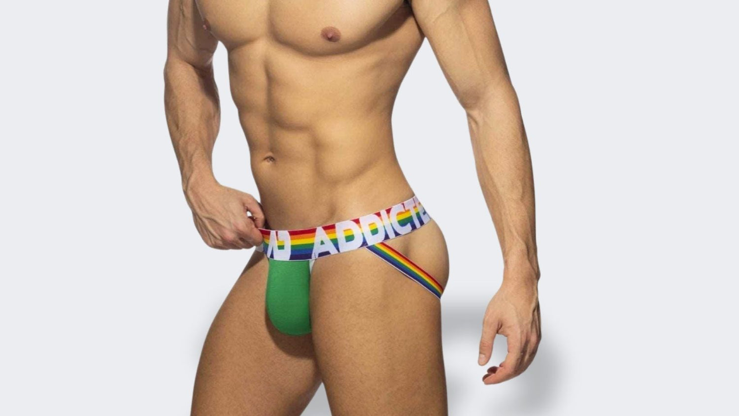 Green ADDICTED Jockstrap with Rainbow Straps – A male model wearing a green jockstrap with rainbow-colored side straps and a waistband branded "ADDICTED" in bold letters. The rainbow accents emphasize pride and individuality.